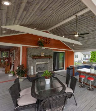 wood paneling in outdoor deck flooring and ceiling with outdoor furniture, fireplace, and kitchen