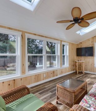 interior wood paneling on floor, ceiling, and walls with furniture a mounted tv and windows
